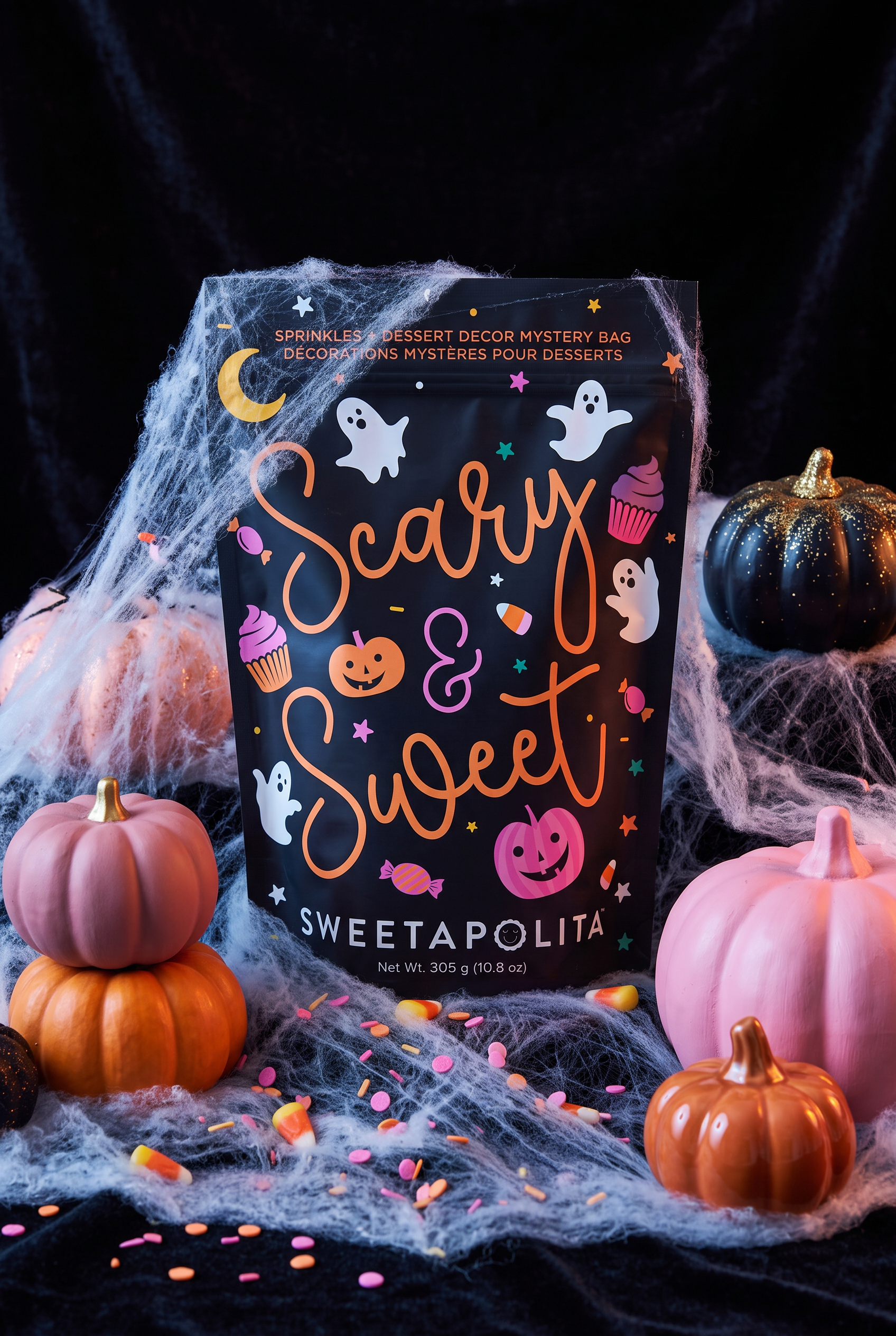 A bag of Sweetapolita 'Scary & Sweet' Halloween-themed dessert and decor mystery bag, styled with fake cobwebs, pink pumpkins, and candy on a black background.